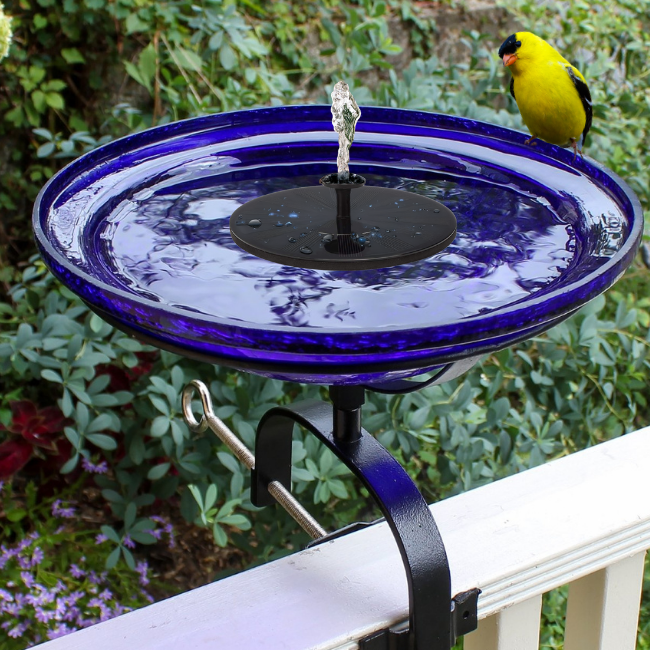 Solar-powered birdbath with a crackle glass bowl and water fountain, attracting a yellow finch perched on the rim.